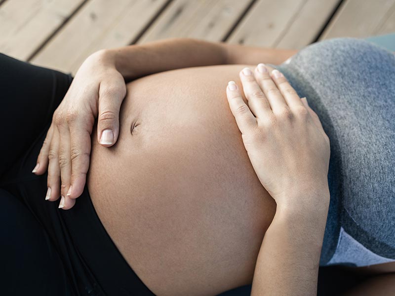 Eine schwangere Frau hält ihre Hände schützend über dem Bauch